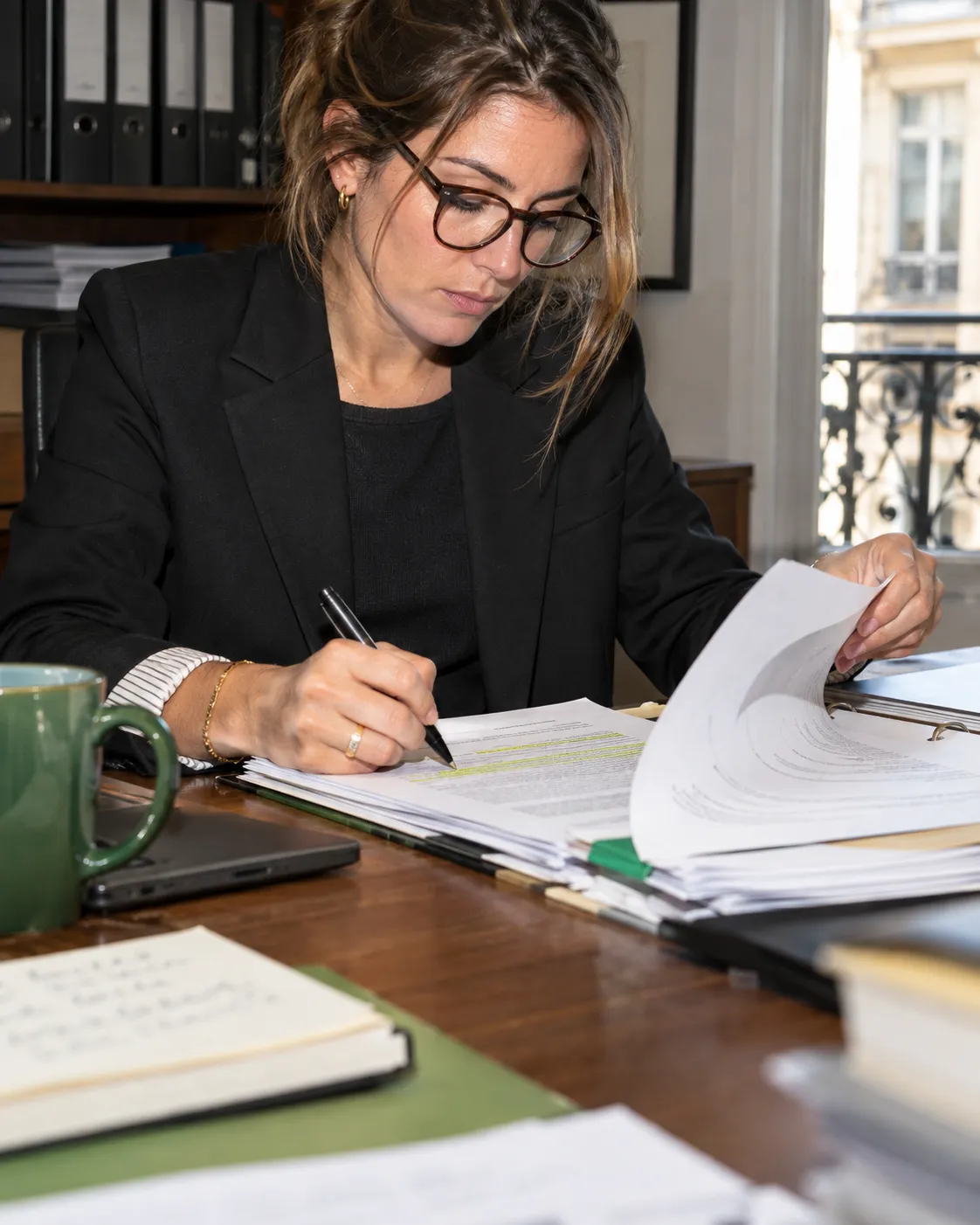 Une avocate relit et annote un dossier papier à son bureau.